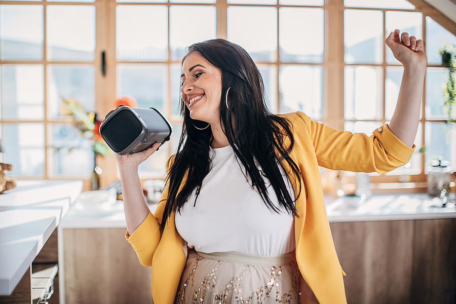 Woman singing and dancing at home and holding wireless bluetooth speaker Photograph by South_agency Woman singing and dancing at home and holding wireless bluetooth speaker Photograph by South_agency