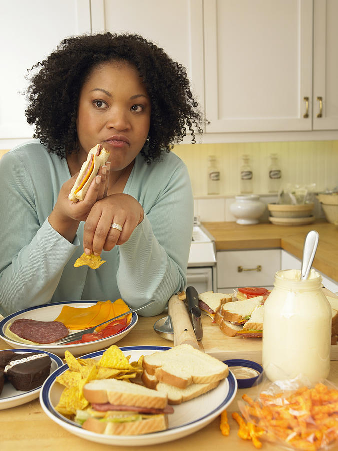 Woman Sits at a Kitchen Table Eating a Lunch of Cheese and Salami Sandwiches and Crisps Photograph by Digital Vision.
