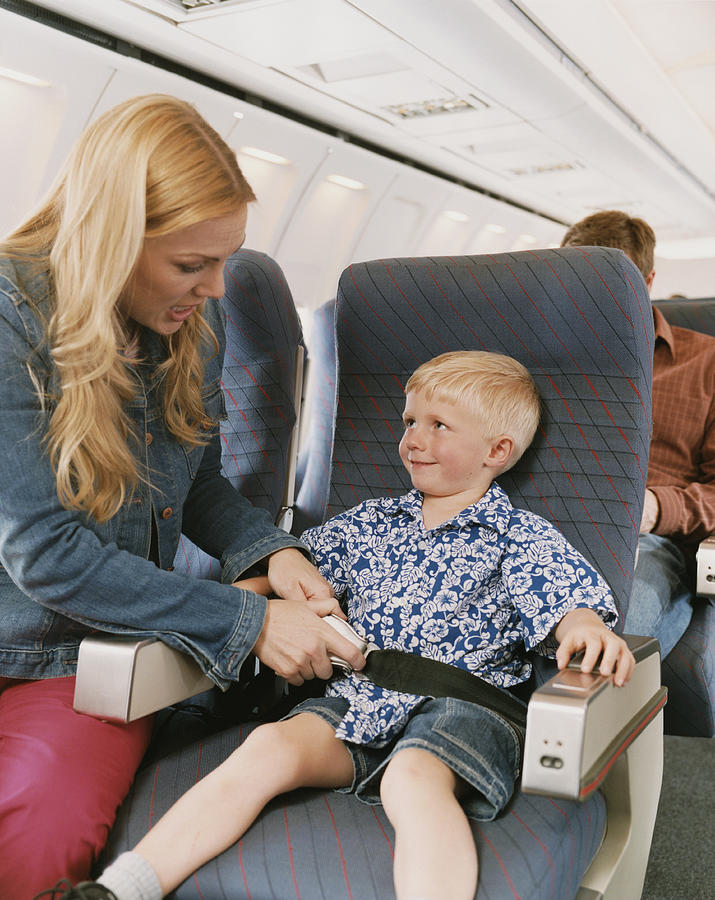 Woman Sits on a Plane With Her Young Son, Adjusting His Seat Belt Photograph by Digital Vision.