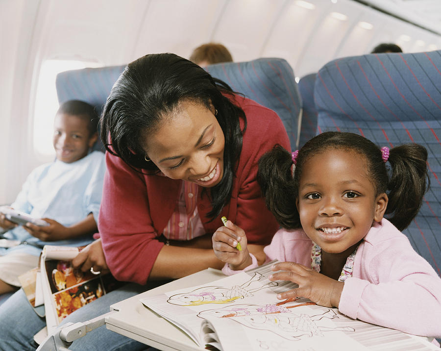 Woman Sits With Her Young Daughter on a Plane, Watching Her Draw in Her Colouring-In Book Photograph by Digital Vision.