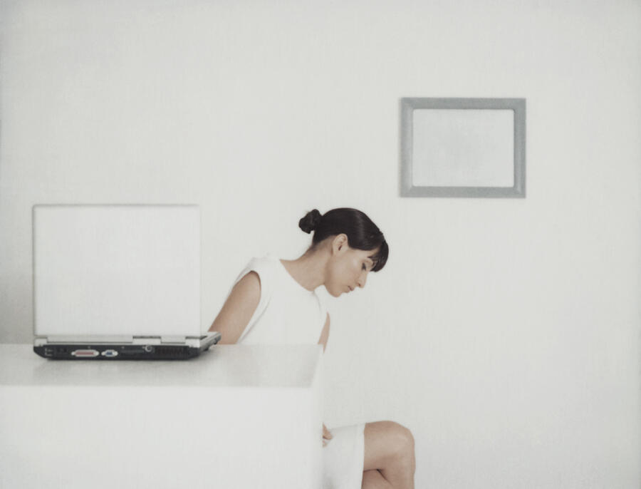 Woman sitting at table with laptop, turning to side and looking down Photograph by Matthieu Spohn