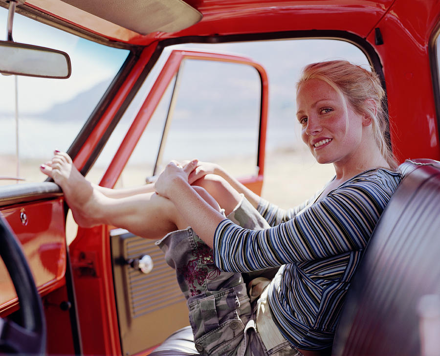 Woman sitting in pick-up truck, resting feet on dashboard, portrait Photograph by Ryan McVay