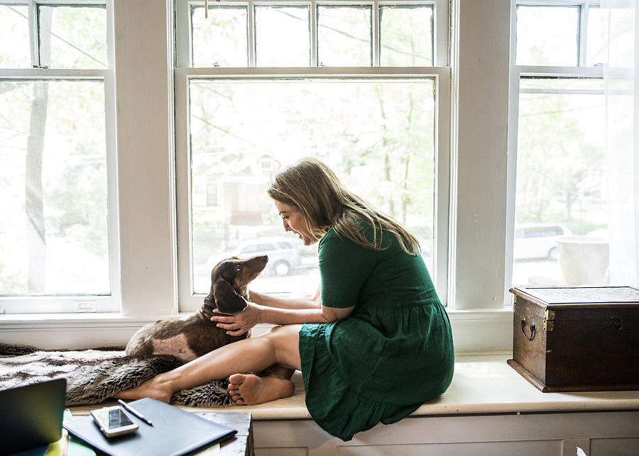 Woman sitting in window with dog Photograph by MoMo Productions