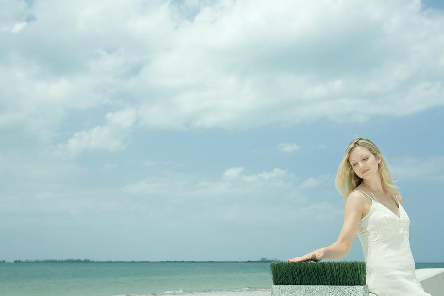Woman sitting near sea, touching blades of wheat grass Photograph by PhotoAlto/Milena Boniek