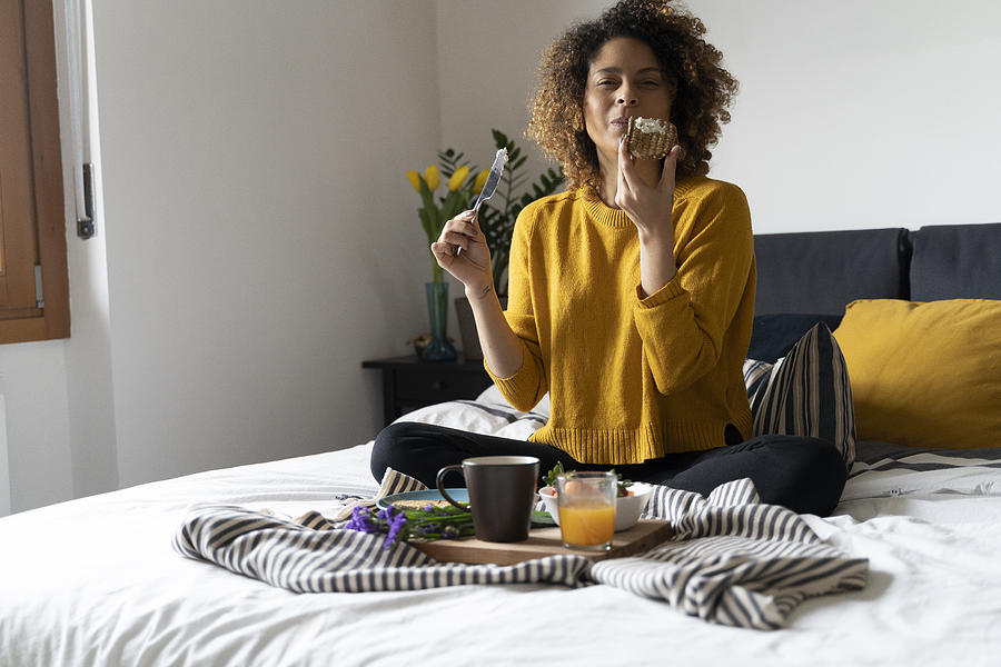 Woman sitting on bed, having a healthy breakfast Photograph by Westend61