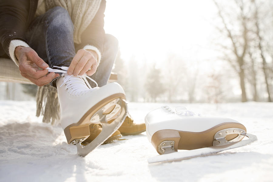 Woman sitting on bench in winter landscape putting on ice skates Photograph by Westend61