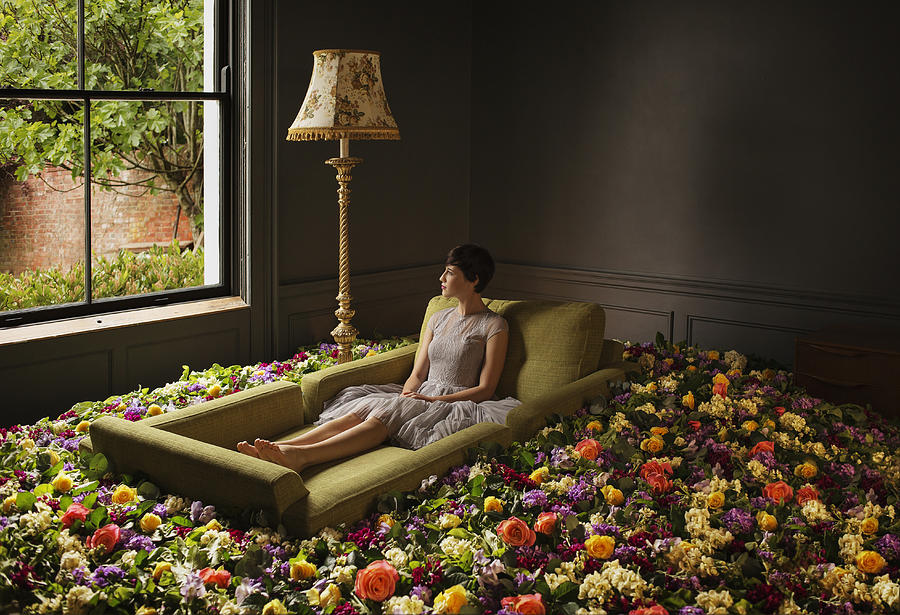 Woman sitting on sofa surrounded by flowers Photograph by Anthony Harvie