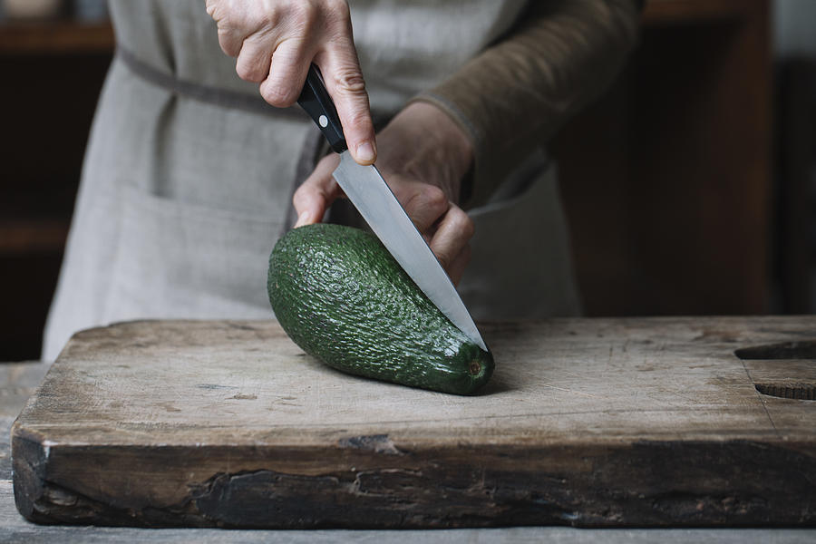 Woman slicing avocado on chopping board, mid section Photograph by Alberto Bogo