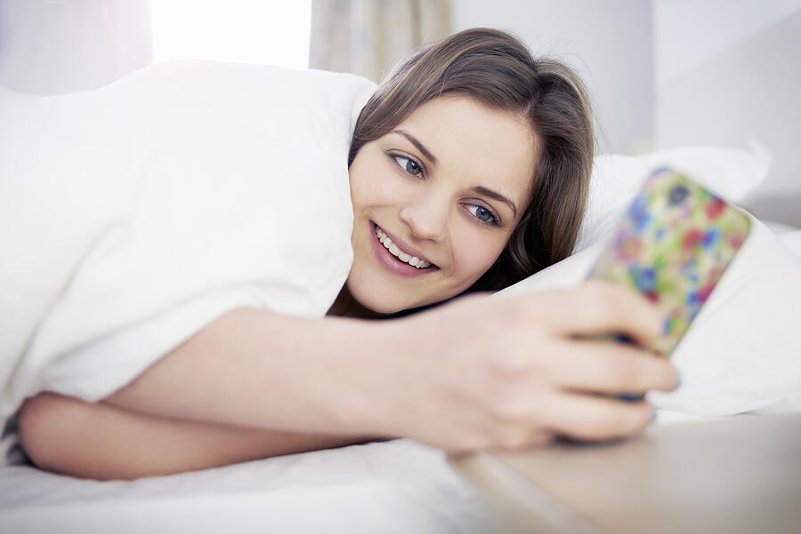 Woman Smiling Looking At Mobile Phone In Bed Photograph by Tara Moore