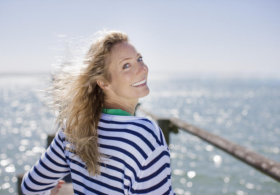 Woman smiling on pier by ocean Photograph by Paul Bradbury