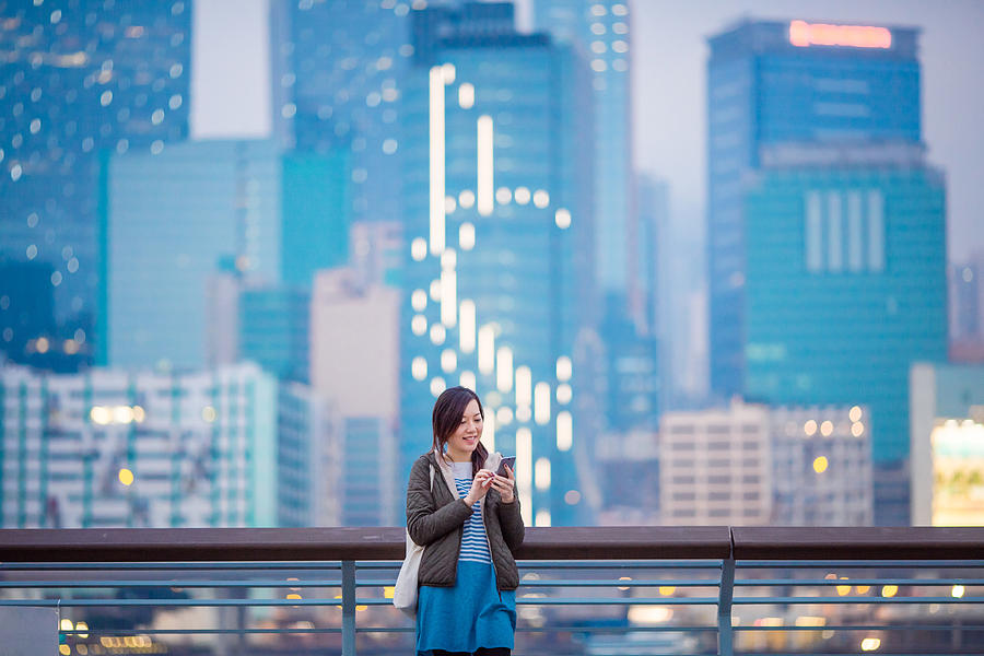 Woman smiling while using smartphone in city Photograph by D3sign