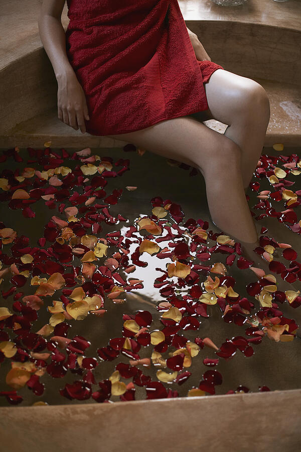 Woman soaking feet in bath with rose petals Photograph by Felix Wirth