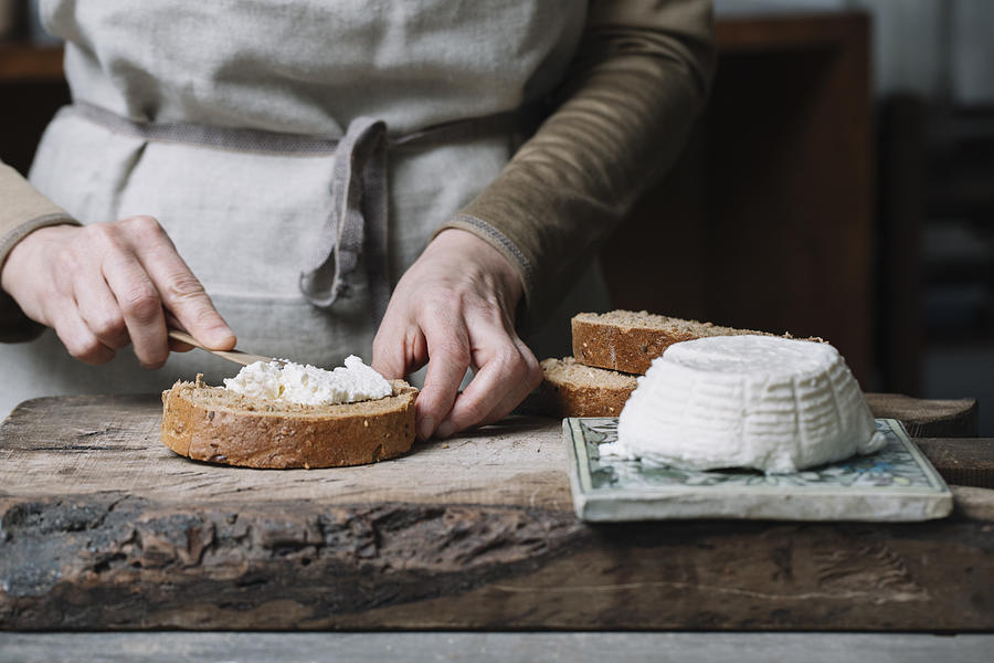 Woman spreading ricotta cheese onto slice of bread, mid section Photograph by Alberto Bogo