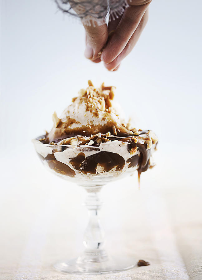 Woman sprinkling nuts on sundae Photograph by Cultura RM Exclusive/Line Klein