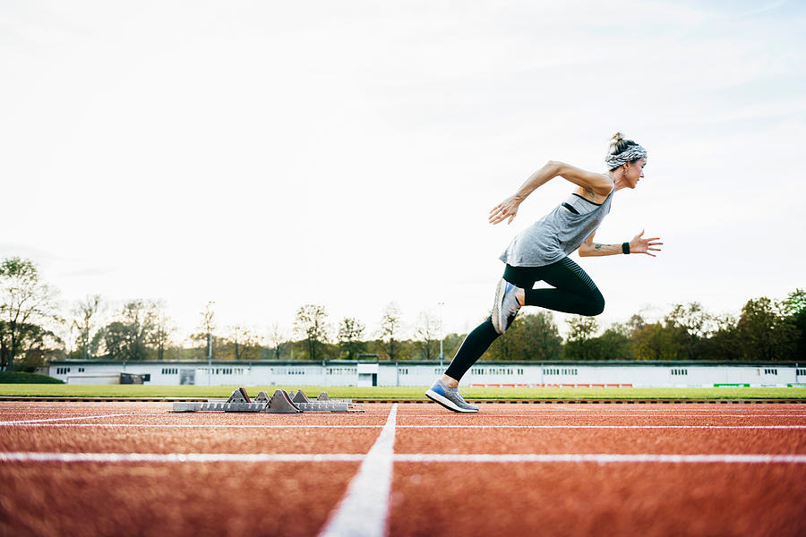 Woman Sprinting Off Starting Blocks On Outdoor Running Track Photograph by Tom Werner