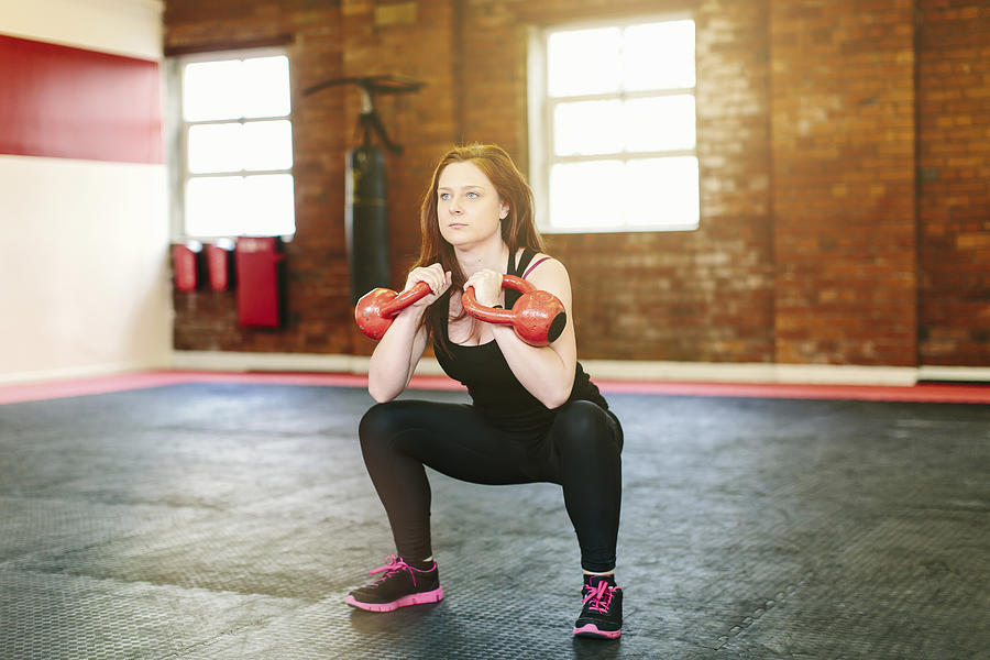 Woman squatting lifting kettlebells Photograph by Mark Webster