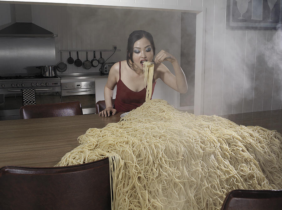 Woman standing at table eating heap of spaghetti Photograph by Nick Dolding