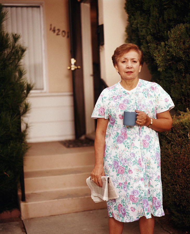 Woman standing in front of house, holding cup and newspaper, portrait Photograph by Ken Chernus