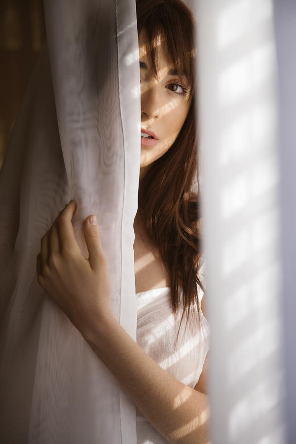 Woman standing in sunlit curtains Photograph by Fotosearch