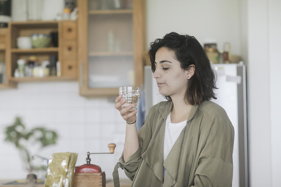 Woman standing in the kitchen drinking a glass of water Photograph by Sigridgombert