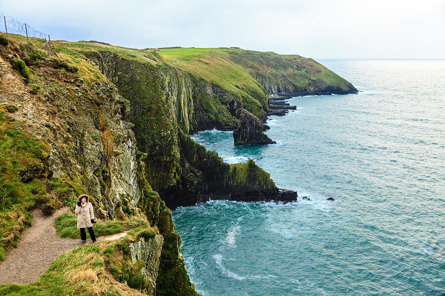 Woman standing on rock cliff by ocean Co. Cork Ireland Photograph by Voyagerix