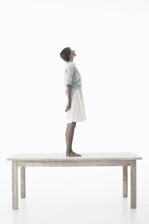 Woman standing on wooden table against white background, side view Photograph by Knowlesie