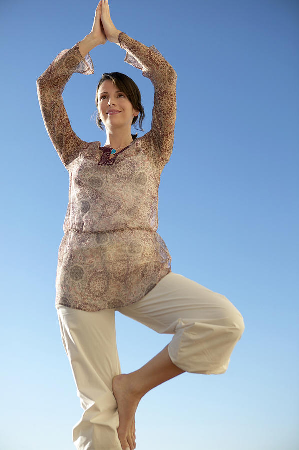 Woman Stands Outdoors in a Yoga Position, On One Leg With Her Arms Above Her Head Photograph by Digital Vision.