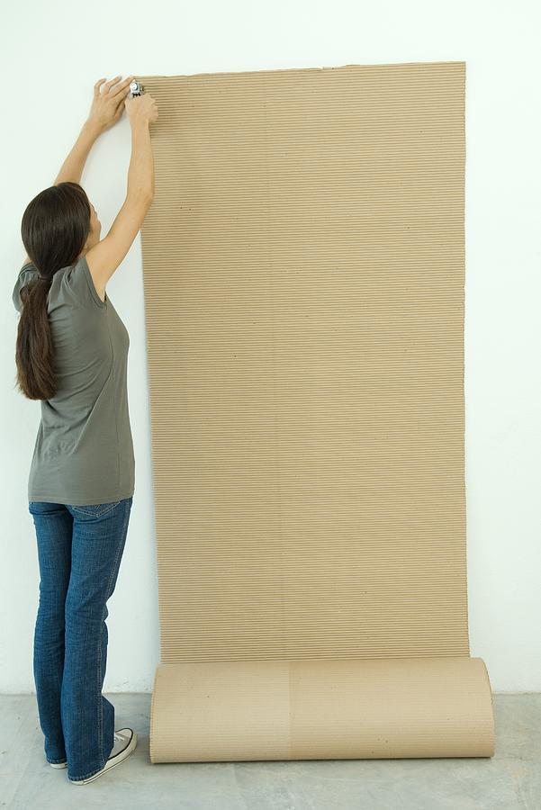 Woman stapling corrugated cardboard to wall Photograph by PhotoAlto/Odilon Dimier