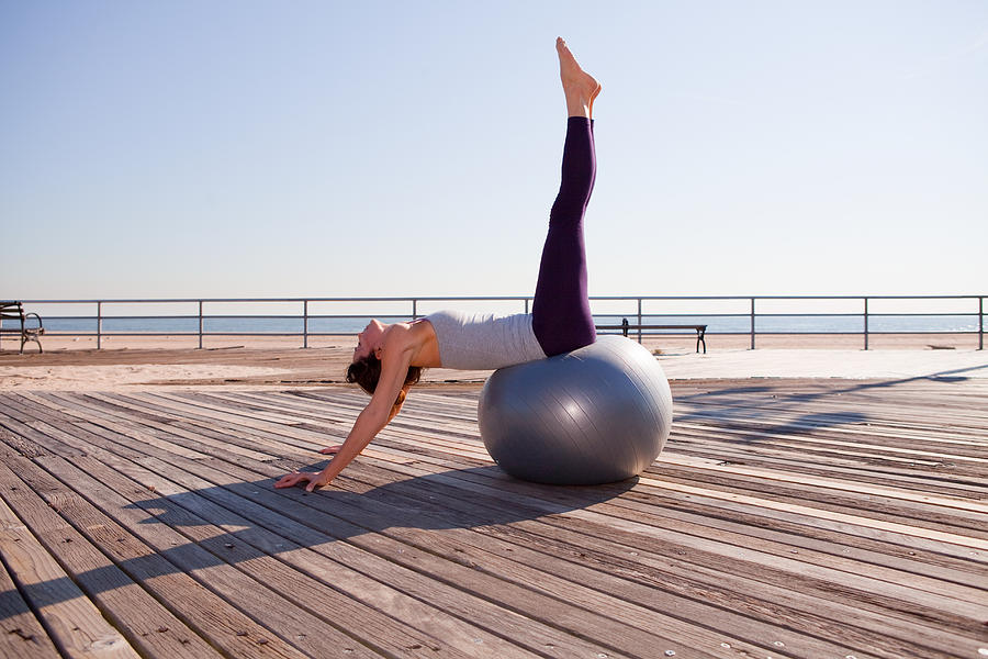 Woman stretching on exercise ball on promenade Photograph by Image Source