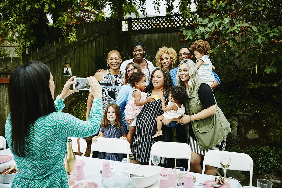 Woman taking photo with smartphone of family Photograph by Thomas Barwick
