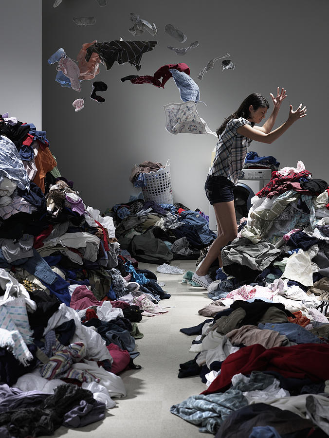 Woman throwing clothes in overflowing laundry room Photograph by Ryan McVay
