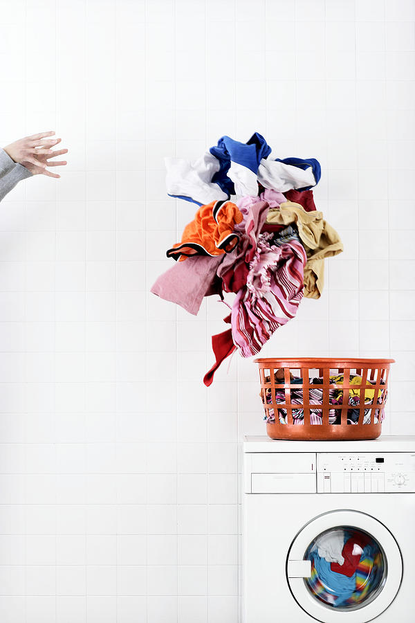 Woman throwing pile of laundry to basket on washing machine Photograph by Martin Poole