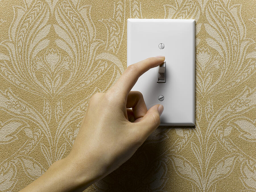 Woman turning off light switch on beige wallpapered wall, close-up Photograph by Jeffrey Hamilton
