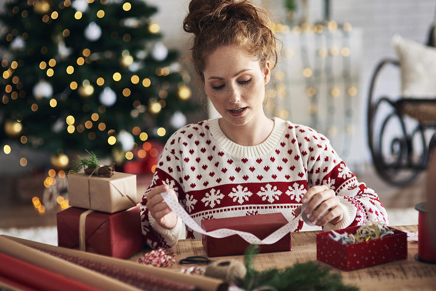Woman tying ribbon on Christmas present Photograph by Gpointstudio