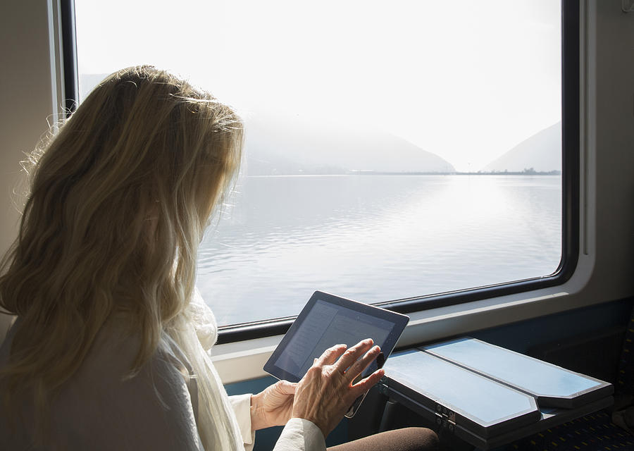 Woman uses digital tablet while riding on train Photograph by Ascent/PKS Media Inc.