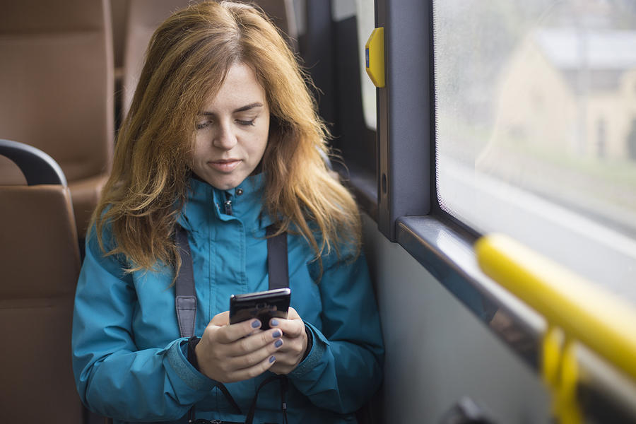 Woman using a mobile phone in a bus Photograph by GoodLifeStudio