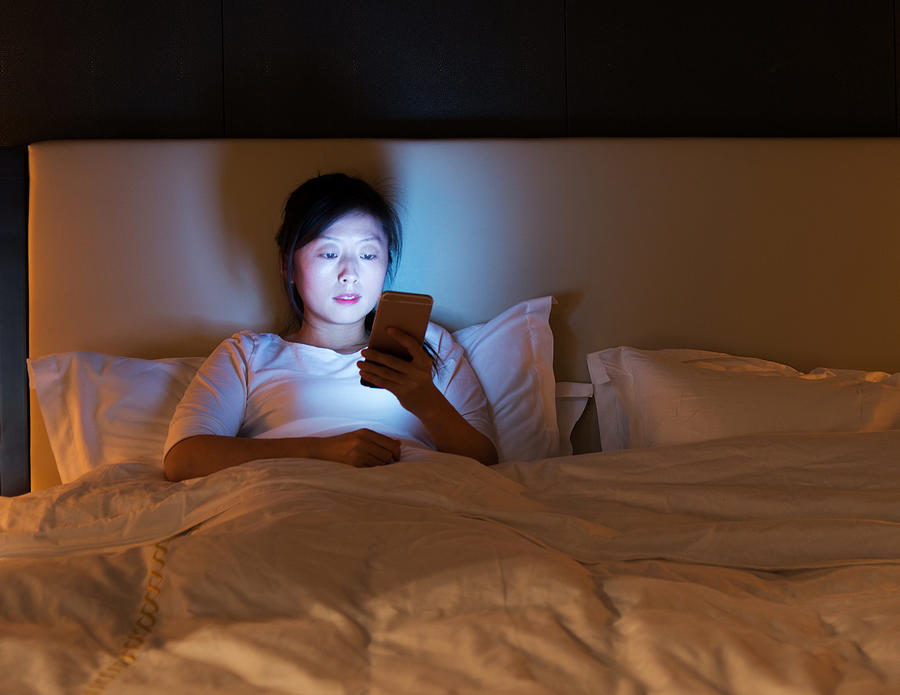 Woman using a smart phone in bed Photograph by Baona
