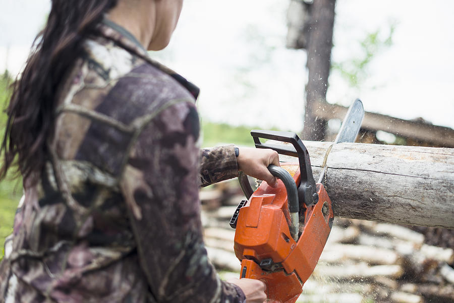 Woman using chainsaw Photograph by Johner Images