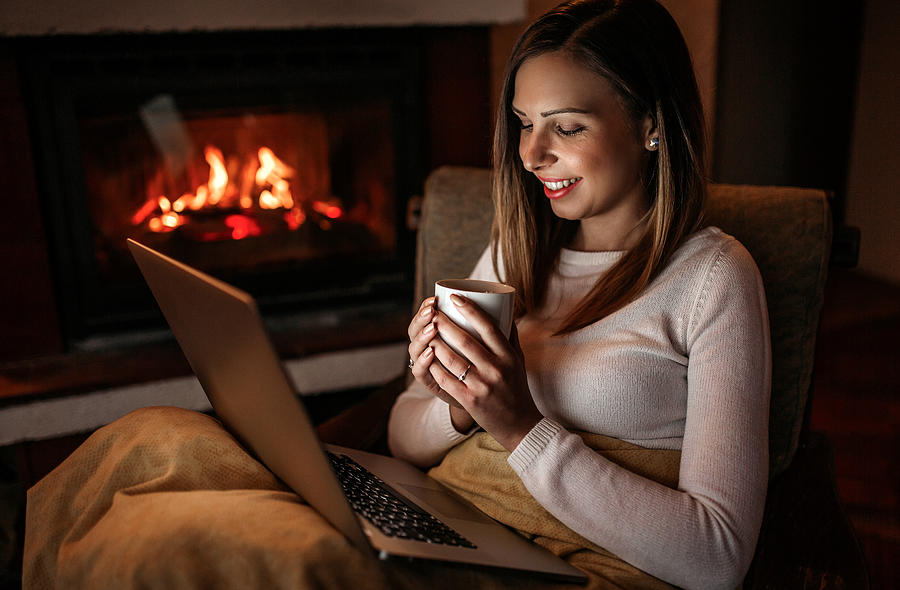 Woman using laptop near fireplace Photograph by CreativeDJ