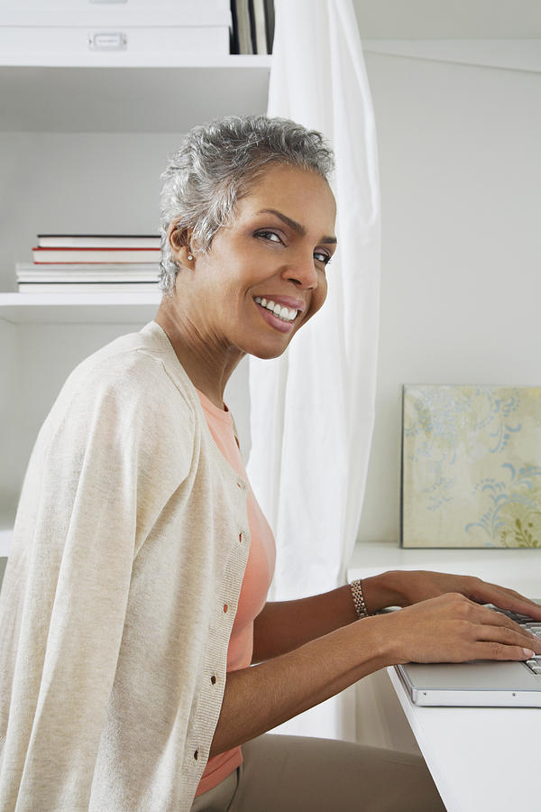 Woman using laptop, smiling, portrait, side view Photograph by Gravity Images