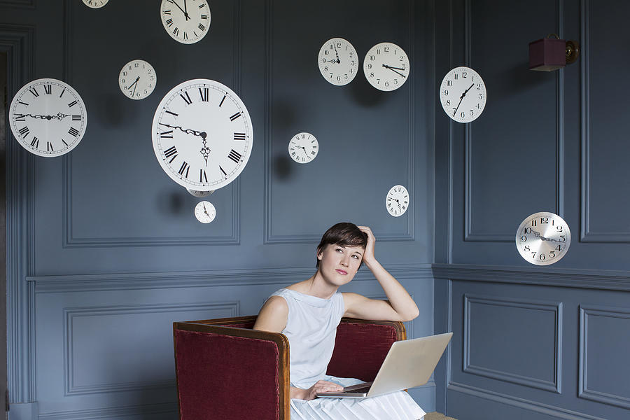 Woman using laptop with hanging clocks above Photograph by Anthony Harvie