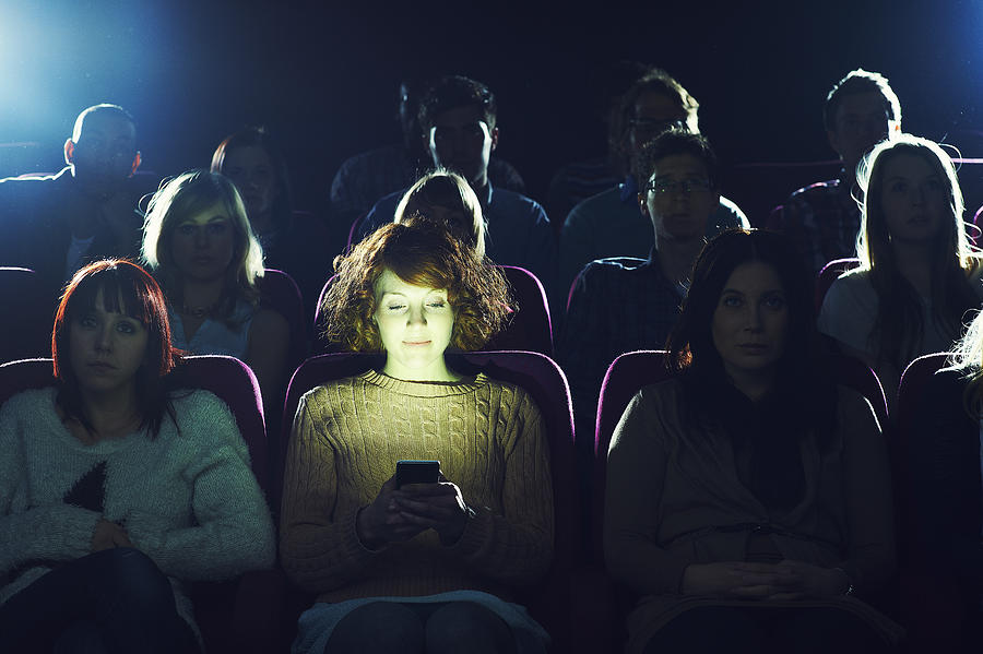 Woman using phone during movie at cinema Photograph by Flashpop