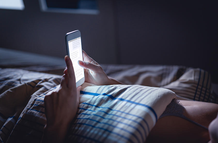 Woman using phone late at night in bed. Person looking at text messages with cell in dark home. Hipster online dating or texting with smartphone. Sexting or cheating concept. Photograph by Tero Vesalainen