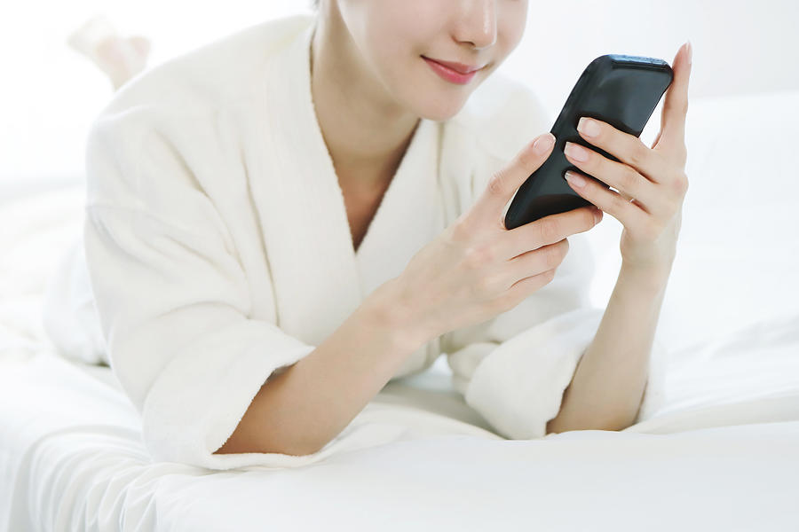 Woman using smartphone on bed Photograph by Runstudio