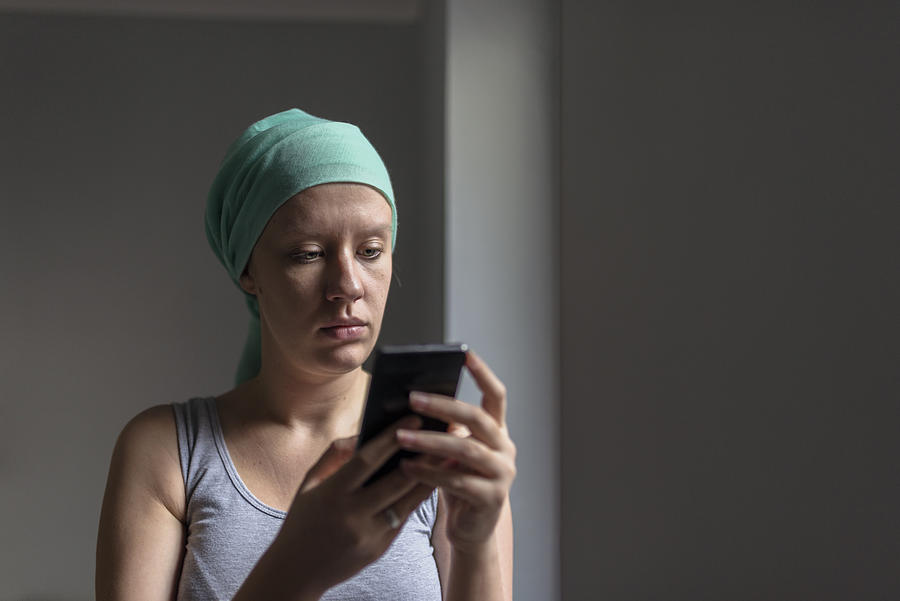 Woman using smartphone while fighting breast Photograph by Ljubaphoto