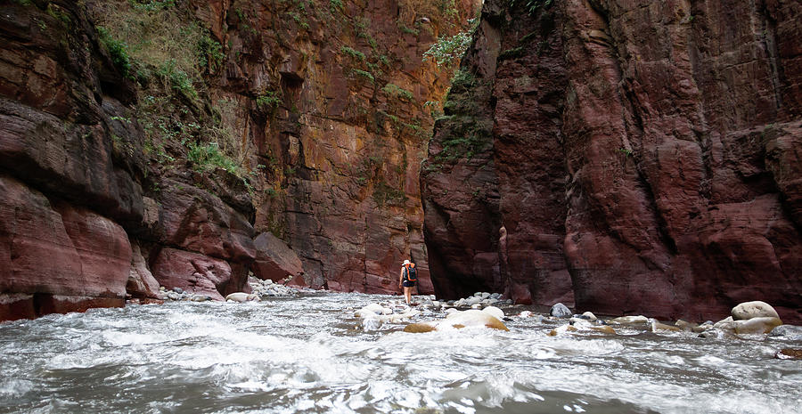 Woman walking in a canyon river between red cliffs in south of France. Photograph by Jean-Luc Farges