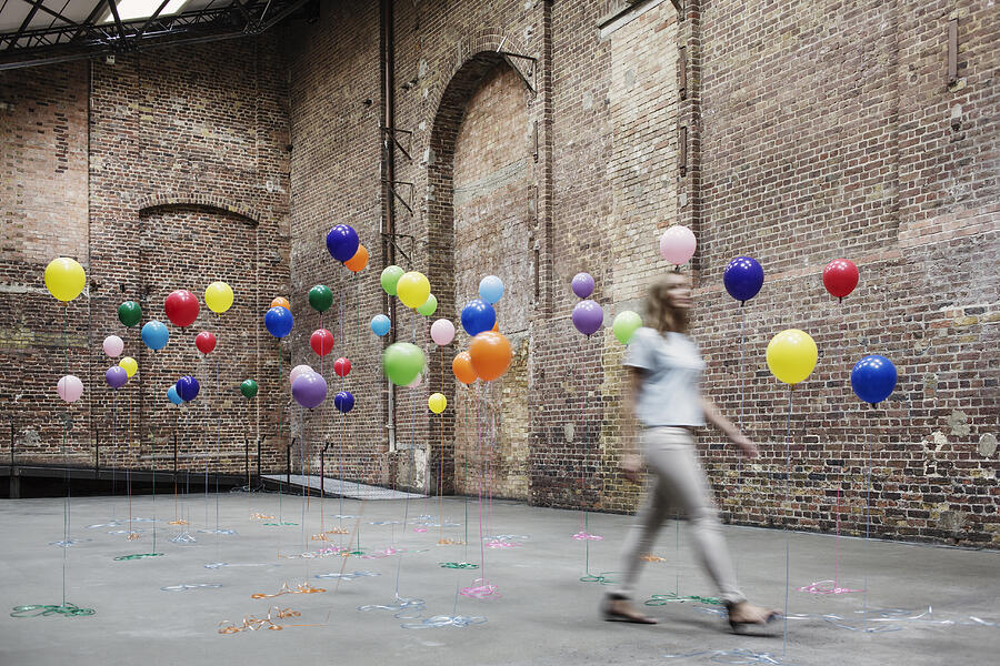 Woman walking in warehouse with colourful balloons Photograph by Anthony Harvie