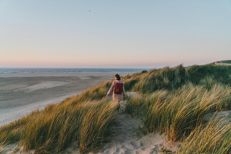 Woman walking near the sea on Texel island  at sunset Photograph by Oleh_Slobodeniuk