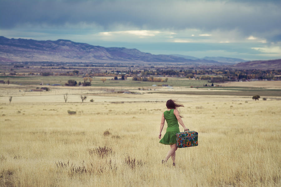 Woman walking with a suitcase searching for home. Photograph by Harpazo_hope
