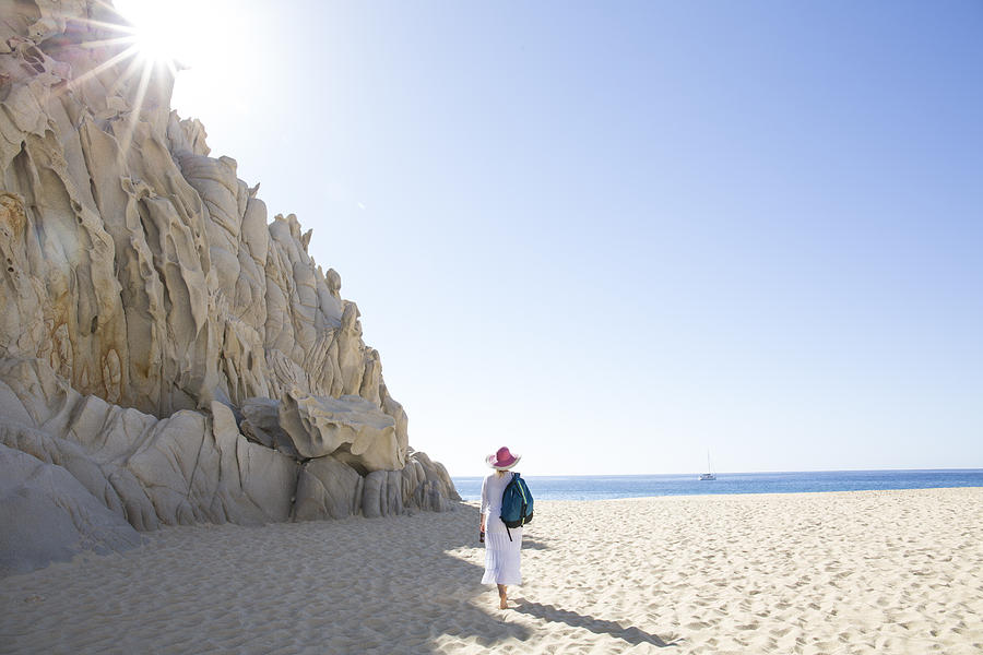 Woman walks along beach below rock cliffs Photograph by Ascent/PKS Media Inc.
